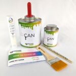 A comprehensive DIY paint touch-up kit is displayed on a white background. The kit includes a large metal can with a red pour spout and a smaller metal can, both labeled "YOU PAINT CAN" and "TOUCH UP DIY KIT" with colorful paint drips. Also present are a white paint pen, a flat paintbrush with a wooden handle and yellow bristles, a wooden stirring stick, and a "HOW TO TOUCH UP USER DIY GUIDE" booklet.
