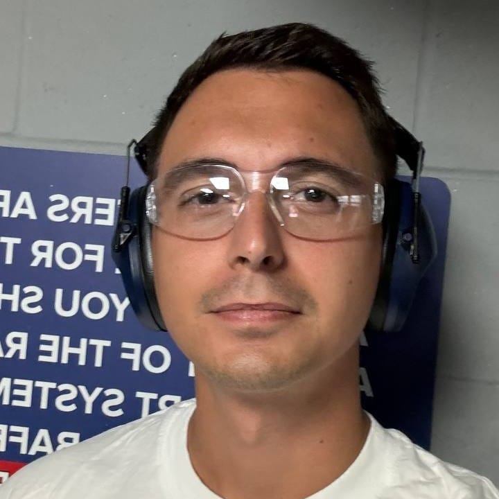 Man in safety glasses and ear protection in front of a blue sign