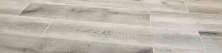 A low-angle perspective shot of light grey and beige wood-look plank flooring with a distressed or whitewashed finish, laid in a staggered pattern.